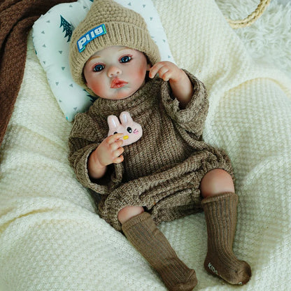 Reborn doll wearing a knit outfit and hat, holding a plush bunny.