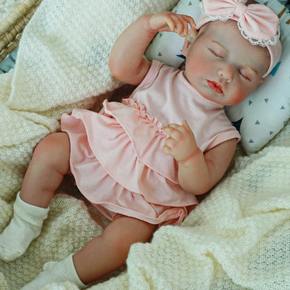 Reborn baby doll laying in a pink dress with socks.