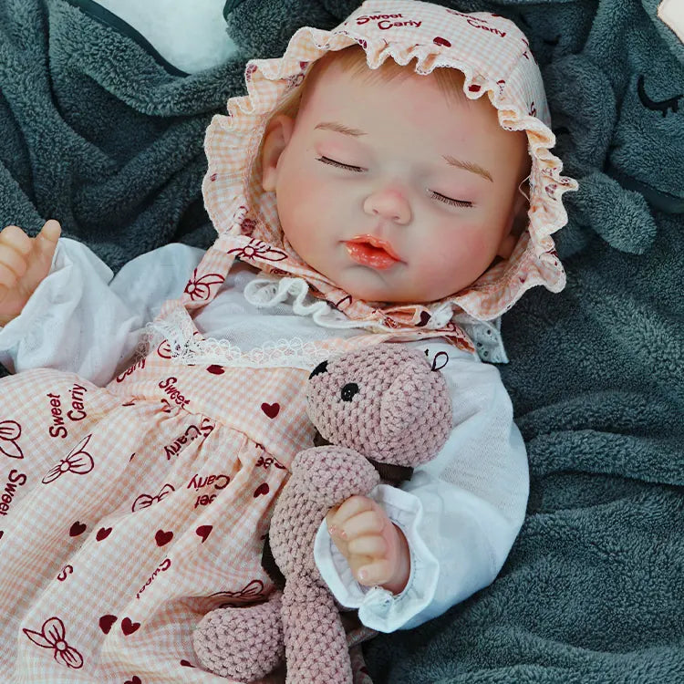 A reborn baby doll peacefully sleeping on a dark blanket, cuddling a pink teddy bear.