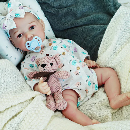 The reborn baby doll with a sweet expression, holding a teddy bear, dressed in a colorful onesie.