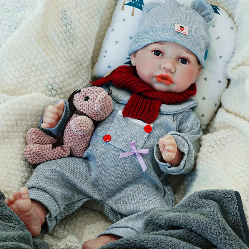 The reborn baby doll sitting contentedly, dressed in a gray onesie and hat, holding a knitted teddy bear.