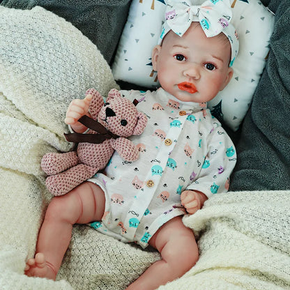 The reborn baby doll with a pacifier, lying down and holding a soft teddy bear.