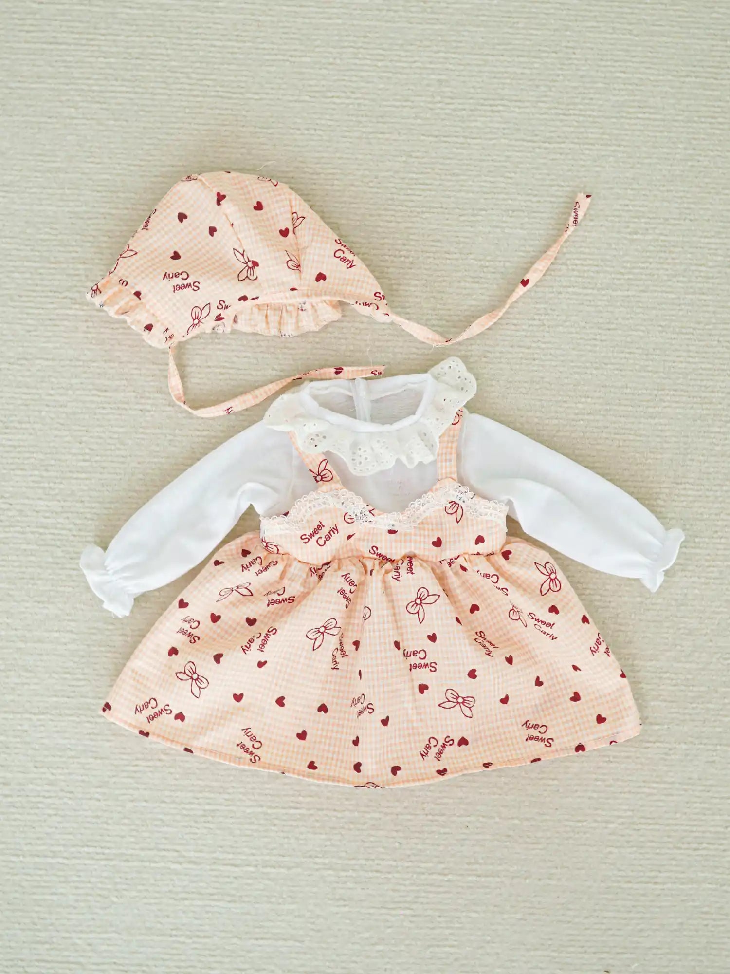 Baby outfit featuring a white blouse with lace details and a pink bonnet and skirt patterned with red hearts and bows.