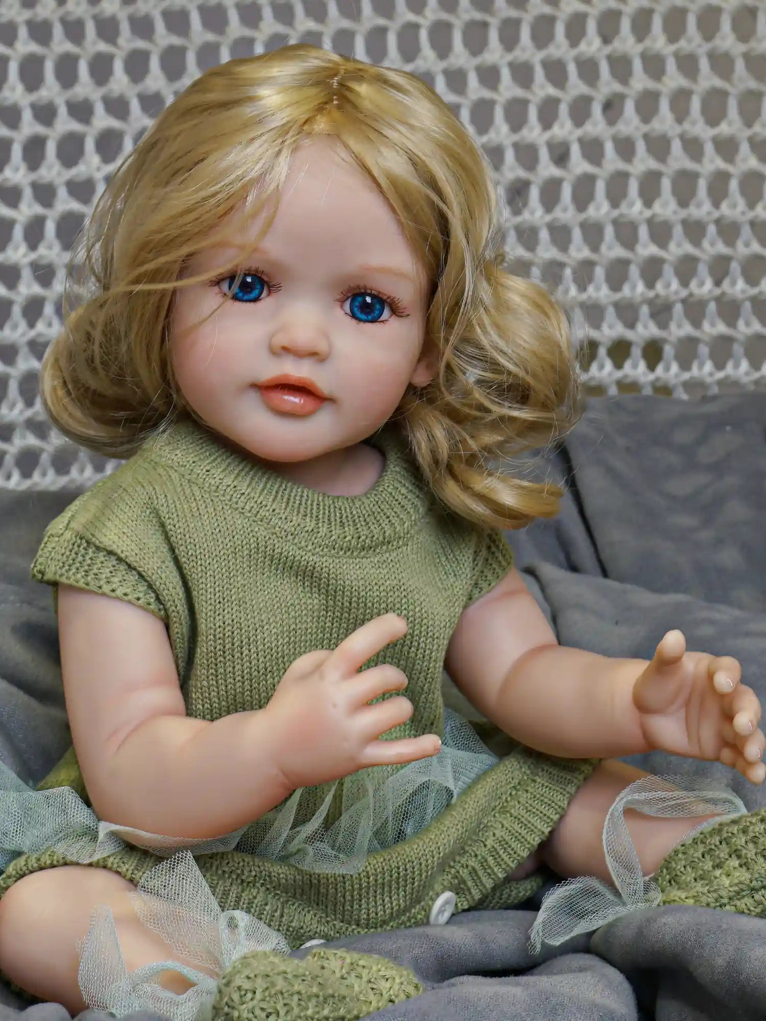 Artisanal doll with the appearance of a young child, featuring blonde curls, sky-blue eyes, and a green hand-knit dress and shoes.