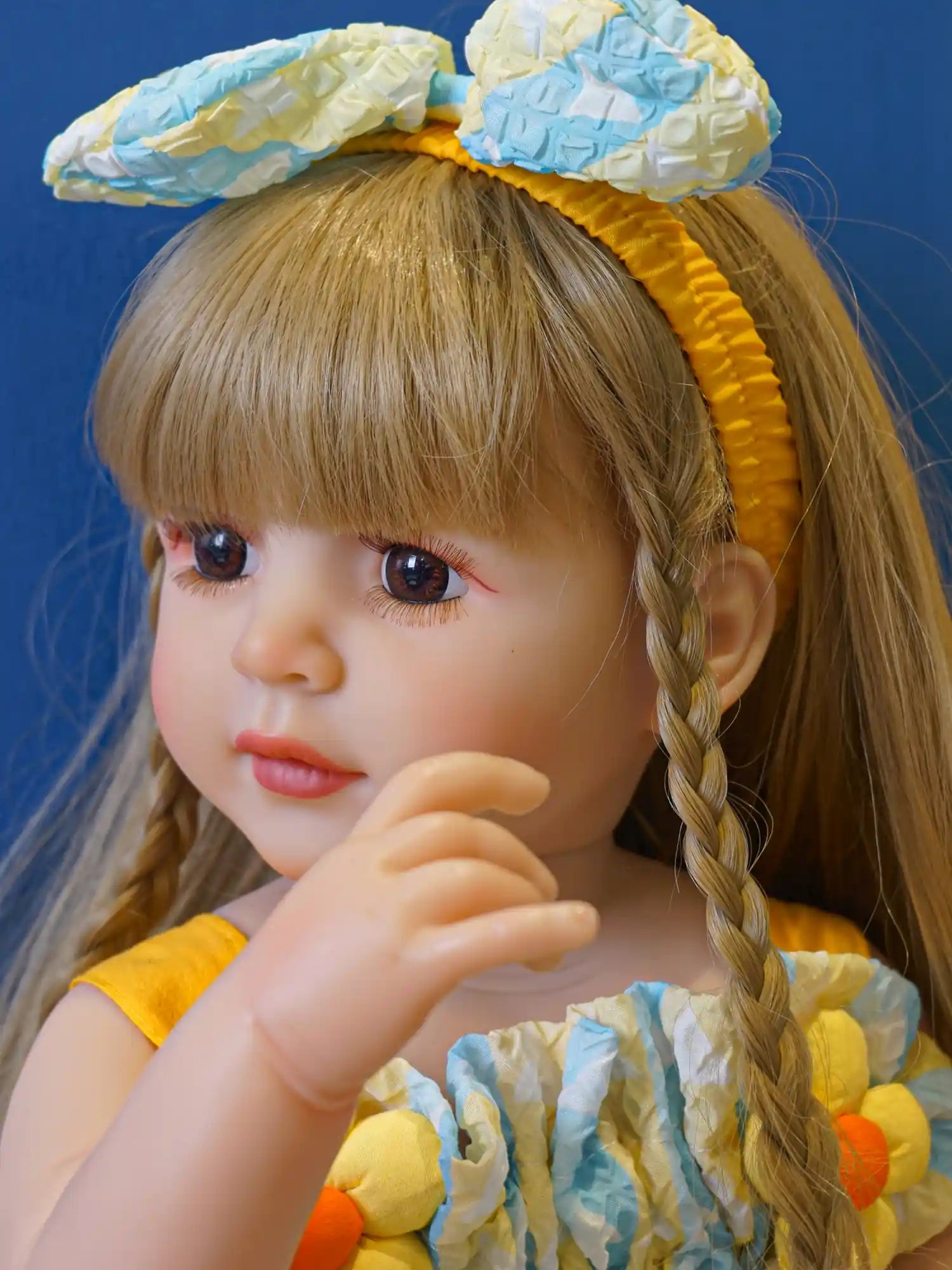 Toddler doll with twin braids and a summer dress, in a relaxed sitting pose.