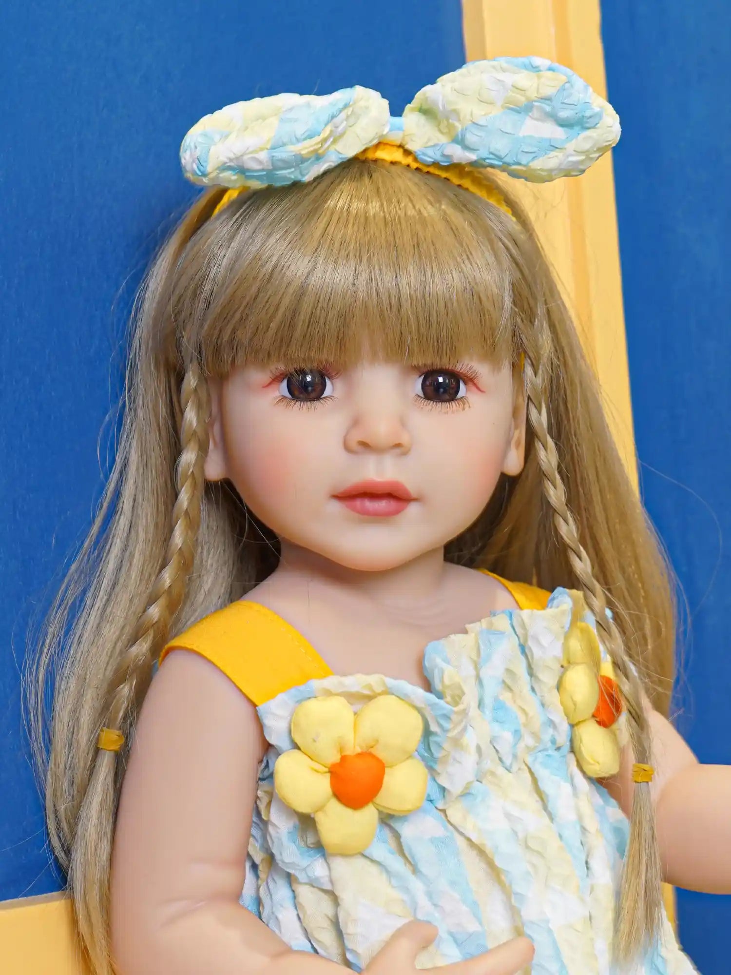A blonde doll in a blue ruffle dress, with matching hairband, seated.