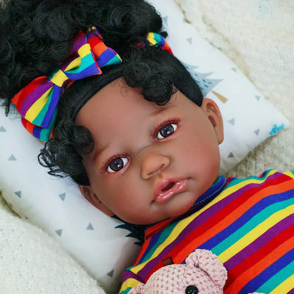 The second image is a close-up of the baby doll's face, highlighting its expression. The doll is wearing a matching rainbow-striped headband and holding the teddy bear.
