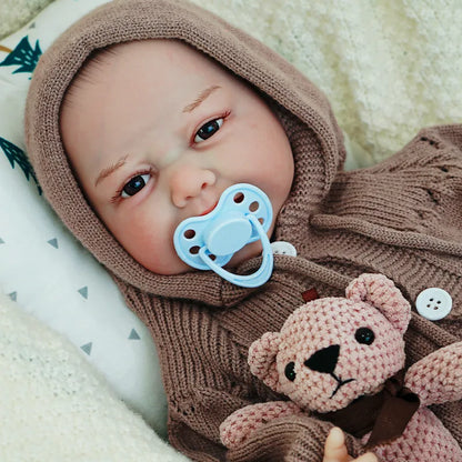 Close-up of the reborn baby doll's face with a pacifier, dressed in a brown knit onesie and hood, looking content.