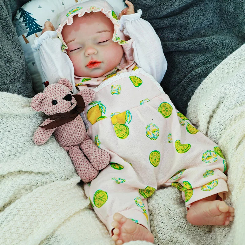 A serene reborn baby doll wearing a bonnet and a green onesie, holding a knitted bear, and resting on a blanket.