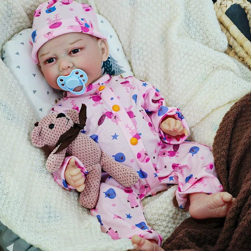 The reborn baby doll with a pacifier, dressed in pink with animal prints, holding a teddy bear while sitting on a blanket.