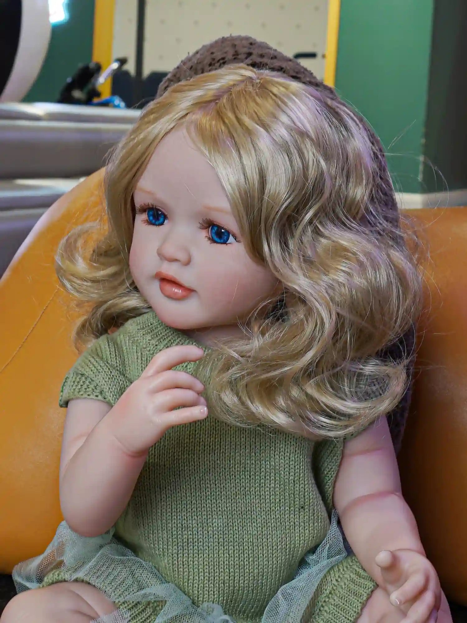 This reborn doll, with her gentle gaze and lush blonde waves, comes adorned in a cozy green garment, ready to be loved and cherished.