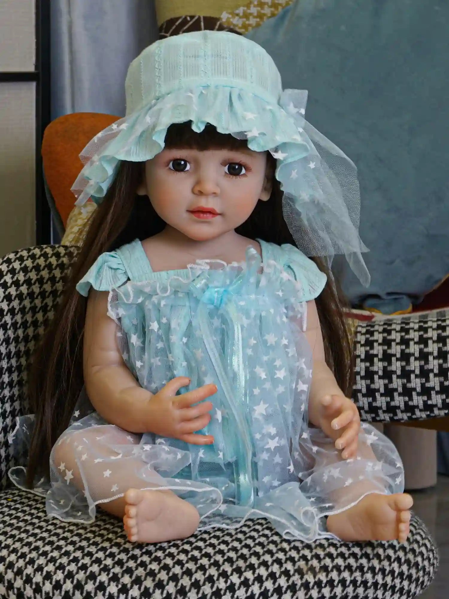 Artisan doll in a delicate blue dress with a bonnet, seated comfortably on a chair.
