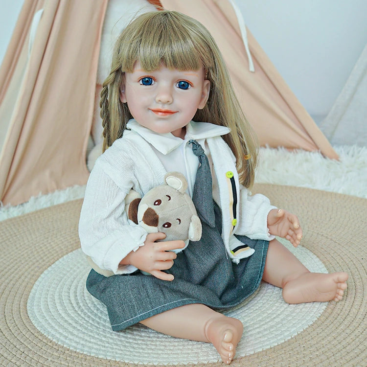 Reborn toddler doll sitting on a soft rug, dressed in a white shirt, gray skirt, and tie, holding a teddy bear.