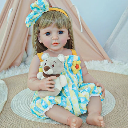 Reborn toddler doll sitting on a soft rug, dressed in a colorful yellow and blue outfit, holding a teddy bear.