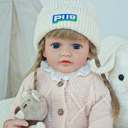 Close-up of a reborn toddler doll wearing a white knit hat and pink coat.