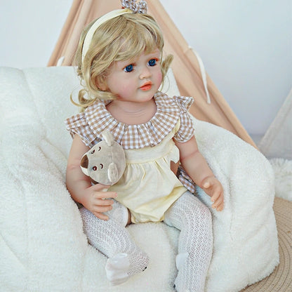  Reborn toddler doll sitting on a rug, dressed in white overalls with a bunny face and holding a small plush toy.