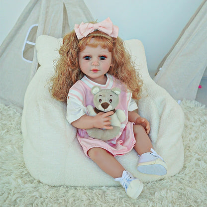 Reborn toddler doll holding a small teddy bear, dressed in a pink outfit with a matching hair bow.