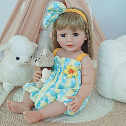  Reborn toddler doll sitting on a soft rug, wearing a bright yellow and blue romper, with her hands resting on her lap.