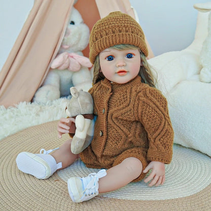 Reborn toddler doll in a brown knit outfit, sitting on a rug with a plush animal in hand.