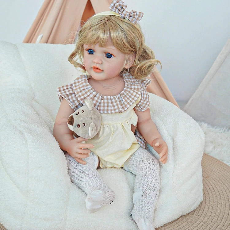 Close-up of reborn toddler doll holding a teddy bear, wearing white overalls with a bunny design and a pink sweater.