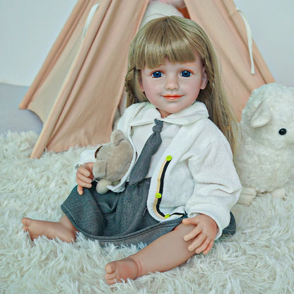 Reborn toddler doll sitting on a soft rug, smiling and holding a teddy bear, dressed in a school-themed outfit.