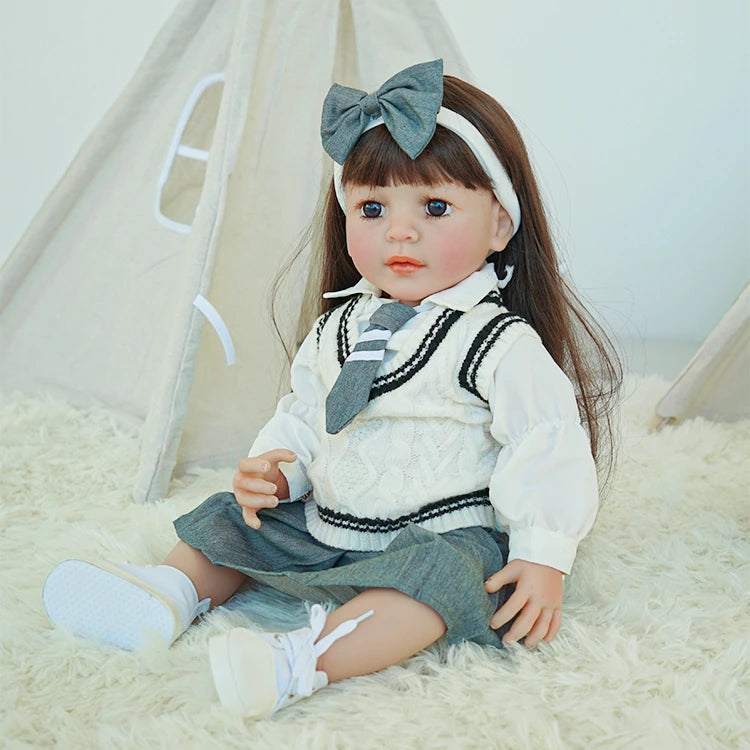 Reborn toddler doll sitting on a soft surface, dressed in a school uniform with a gray skirt and matching headband bow.