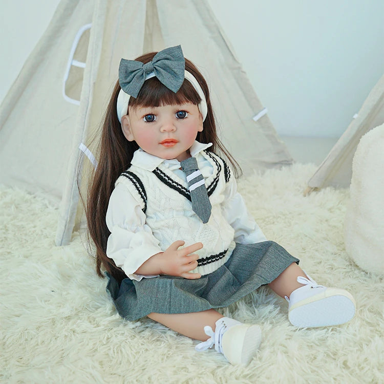 eborn toddler doll sitting on a soft white rug, wearing a school-themed outfit with a gray skirt and a large bow.