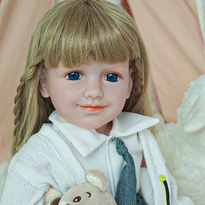 Close-up of reborn toddler doll smiling, with blonde braids, wearing a white shirt and gray tie, holding a plush bear.