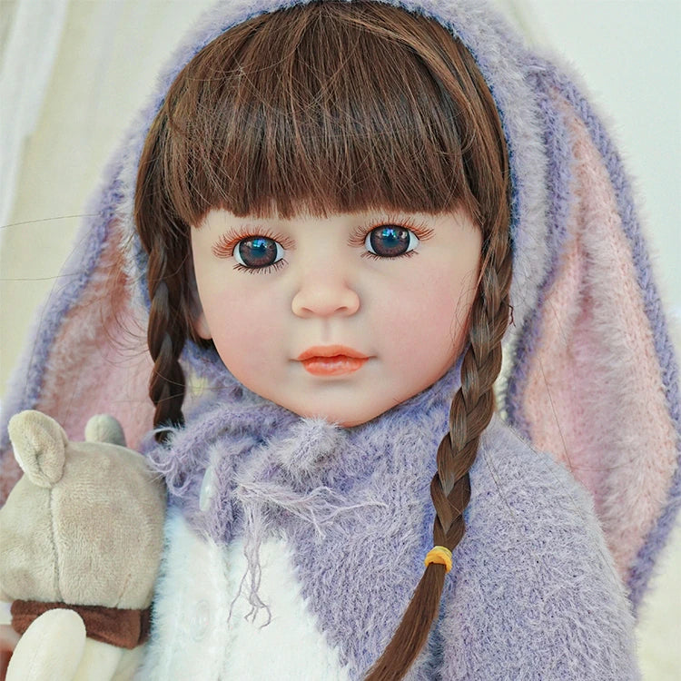 Close-up of reborn toddler doll with long brown hair and braids, dressed in a bunny-themed purple outfit and holding a plush toy.