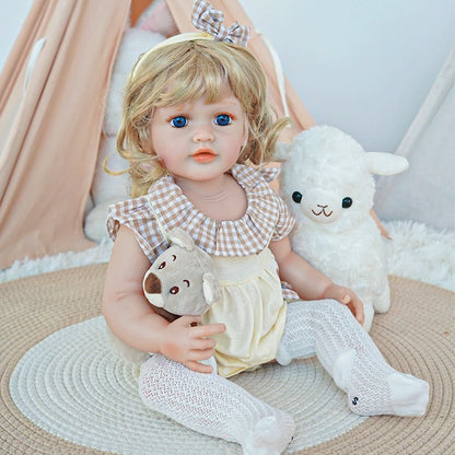 Reborn toddler doll sitting on a plush chair, dressed in pink and white, holding a teddy bear in her arms.