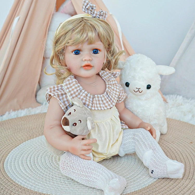 Reborn toddler doll sitting on a plush chair, dressed in pink and white, holding a teddy bear in her arms.