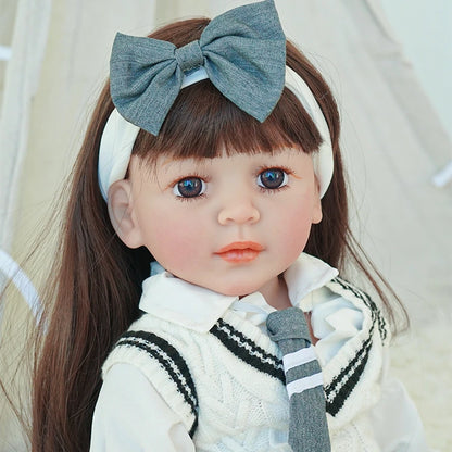 Close-up of reborn toddler doll with long brown hair, wearing a white and gray school uniform with a large gray bow in her hair.