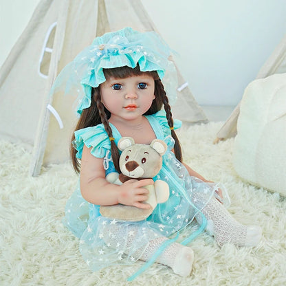 Reborn toddler doll wearing a light blue dress with polka dots and matching bonnet, sitting on a soft rug.