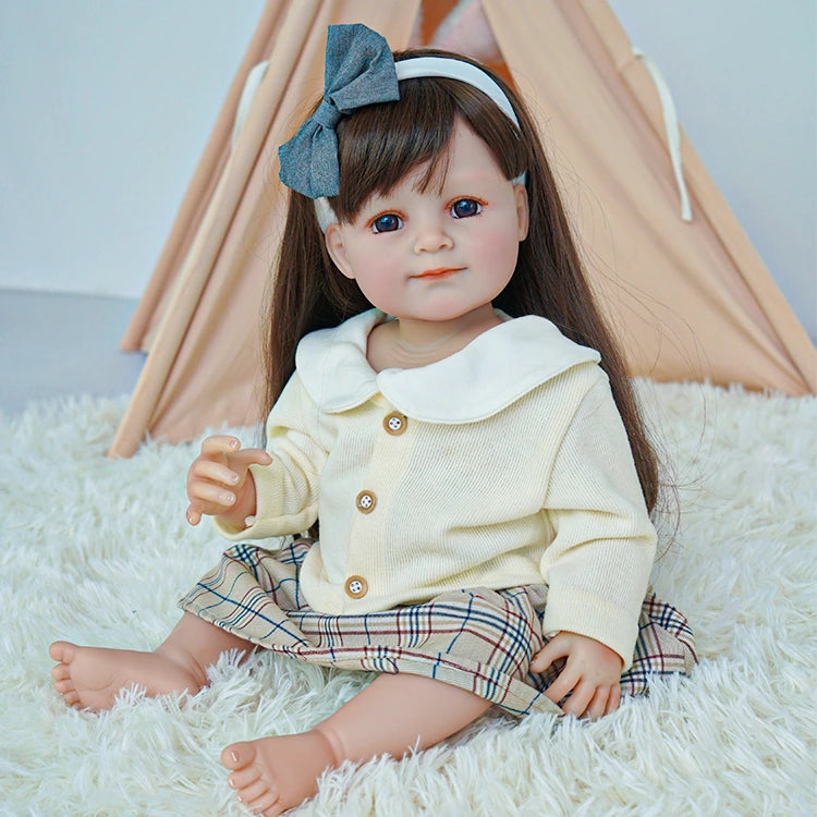  Reborn toddler doll sitting on a soft rug, wearing a plaid skirt and cream sweater, holding a small teddy bear.