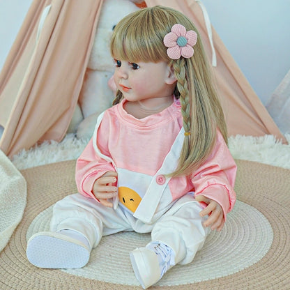 Reborn toddler doll sitting on a soft rug, looking to the side, dressed in a pink and white outfit with a flower clip.