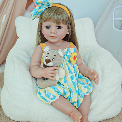 Reborn toddler doll sitting in a cozy chair, wearing a bright and colorful romper, holding a small teddy bear.