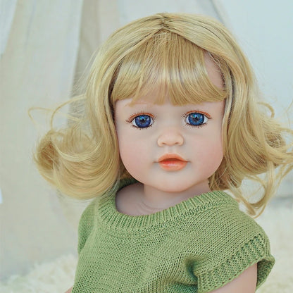 Close-up of a reborn toddler doll wearing a green knit outfit with blonde curly hair and blue eyes.