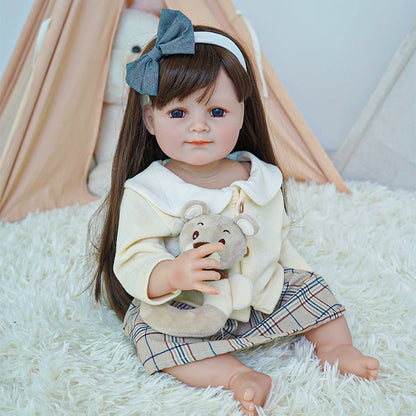 Reborn toddler doll sitting on a rug, wearing a cream cardigan and plaid skirt, holding a teddy bear with a gentle expression.