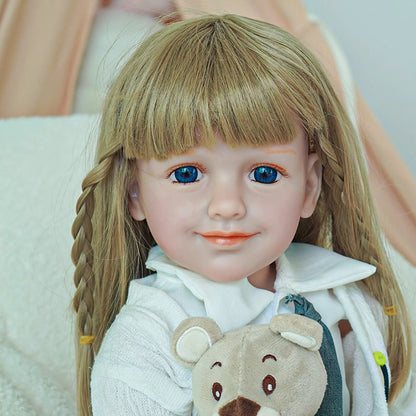 Close-up of reborn toddler doll smiling, holding a plush bear, dressed in a white shirt and gray tie.