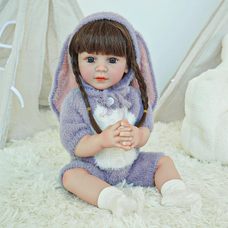 Reborn toddler doll sitting on a soft rug, dressed in a fluffy purple bunny outfit with long ears.