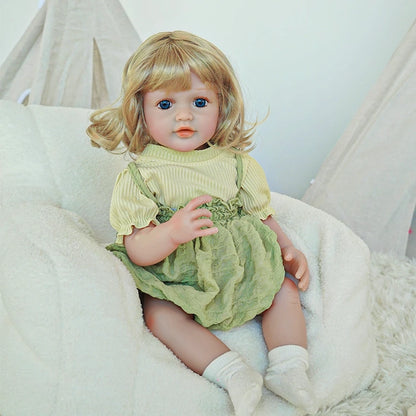 Close-up of reborn toddler doll with blonde curls, wearing a light green dress, looking straight ahead.