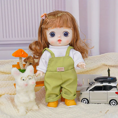 Doll with chestnut hair and blue eyes in a white shirt and green overalls, next to a fluffy toy cat.