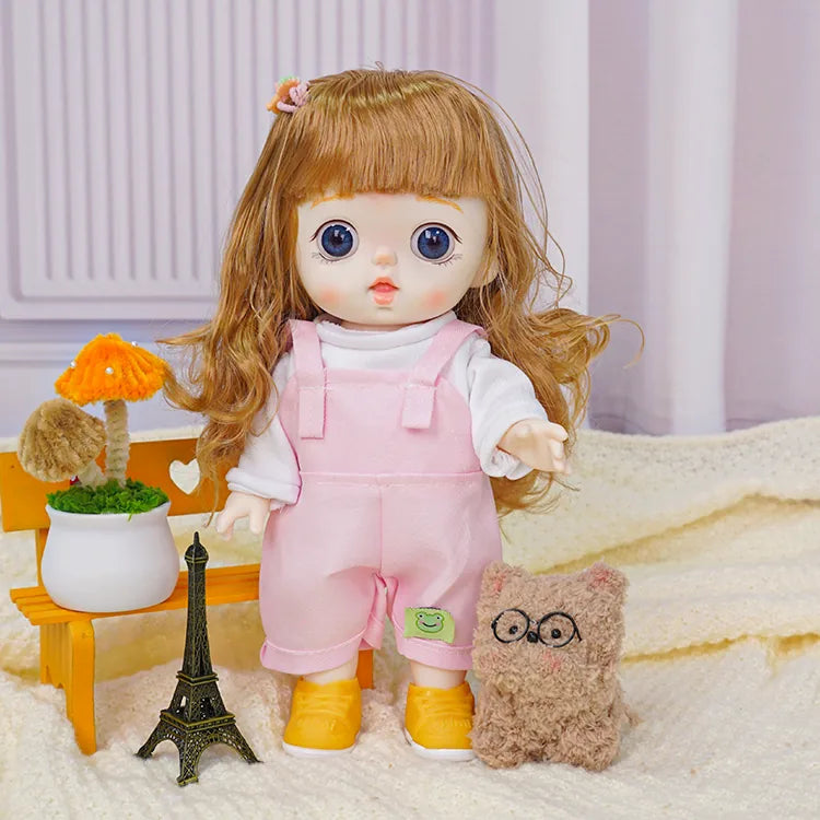 Sweet doll with a side hair clip, dressed in soft pink overalls, next to a brown plush toy and a tiny Eiffel Tower.