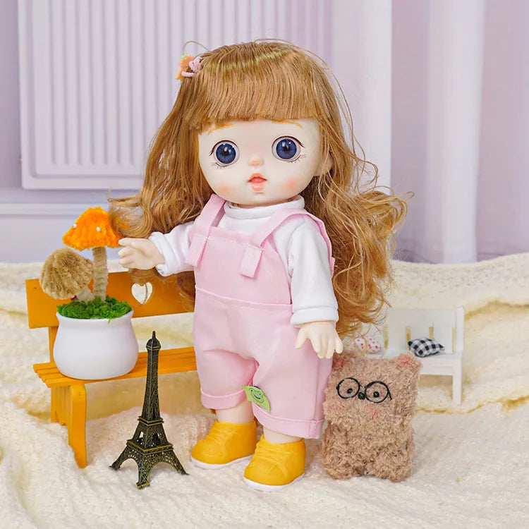 Child-like doll in a pink outfit with a frog patch, with a cuddly toy friend and a small black Eiffel Tower replica.