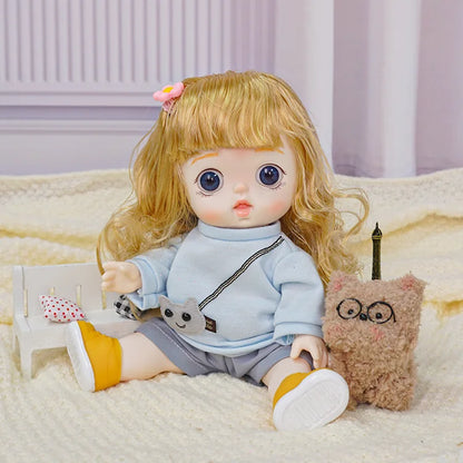 A little doll with wavy hair and a playful expression, wearing casual play clothes and standing near a soft, bespectacled toy.