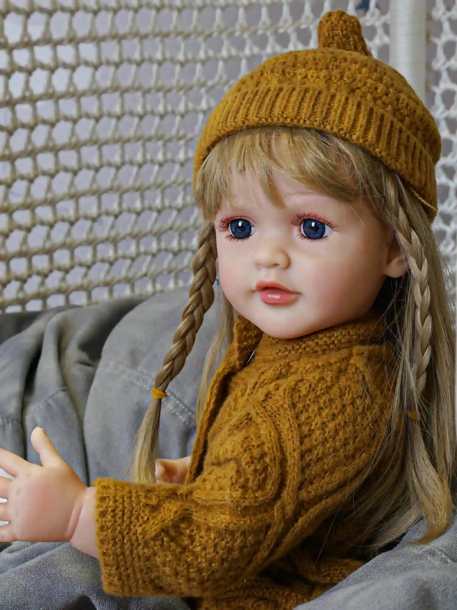 This reborn doll, with strands of gold in her hair and a tender expression, dressed in an olive-hued knit, is a heartwarming addition to any collection.